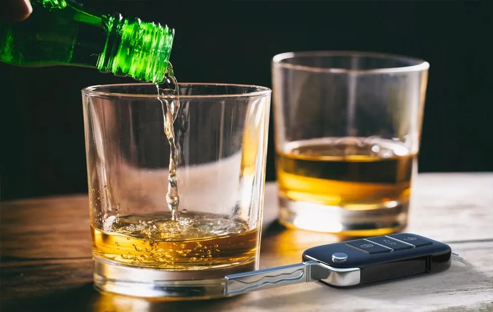 Bei Alkohol am Steuer drohen hohe Strafen Ein Autoschlüssel liegt neben zwei Gläsern Cognac auf einem Holztisch